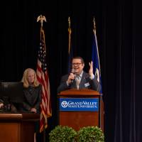 Man in suit gesticulates behind podium on stage
